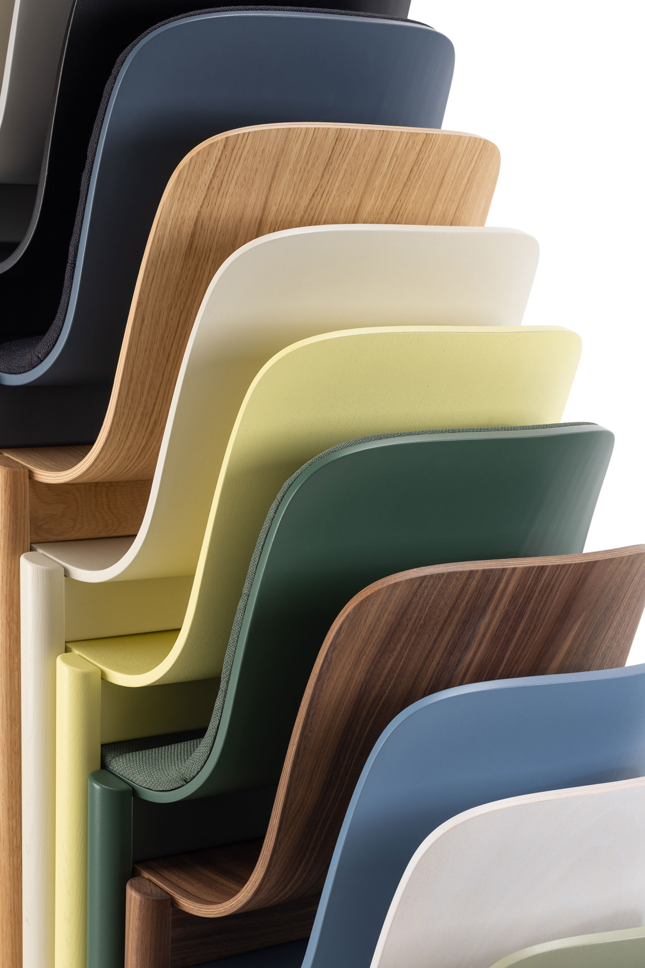 A stack of multiple All’essenza chairs in different wood finishes and colors.