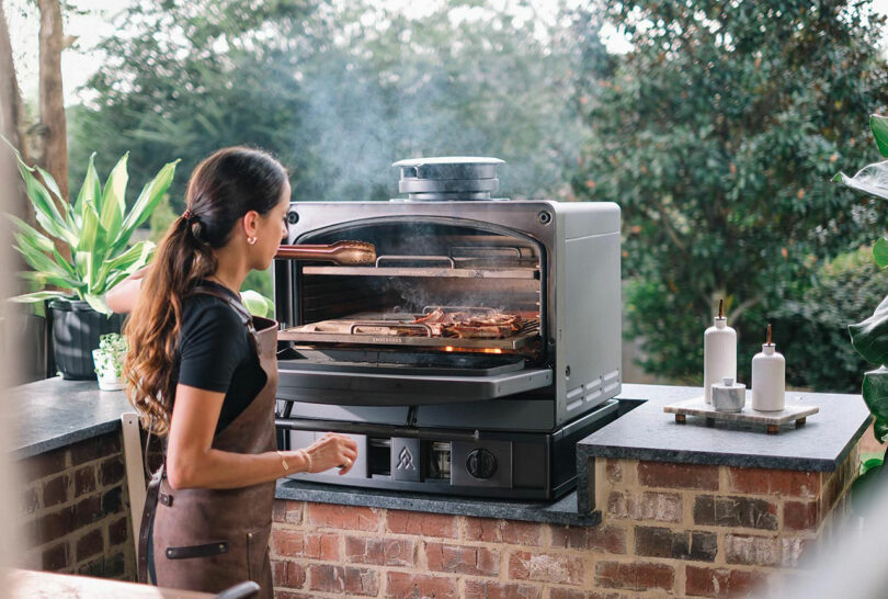A chef using the Emberhaus oven in an outdoor kitchen with visible smoke from live-fire cooking.