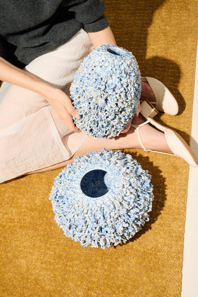 A person holding a textured, blue and white 3D-printed ceramic sculptural object to show scale and detail.