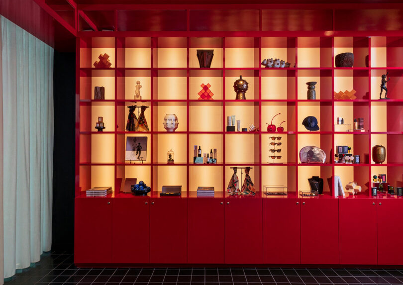 A vibrant red lacquered shelving unit with illuminated cubbies displaying decorative objects.