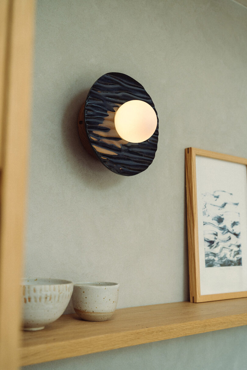 A round wall sconce with a dark ebonised wooden base and glowing bulb.