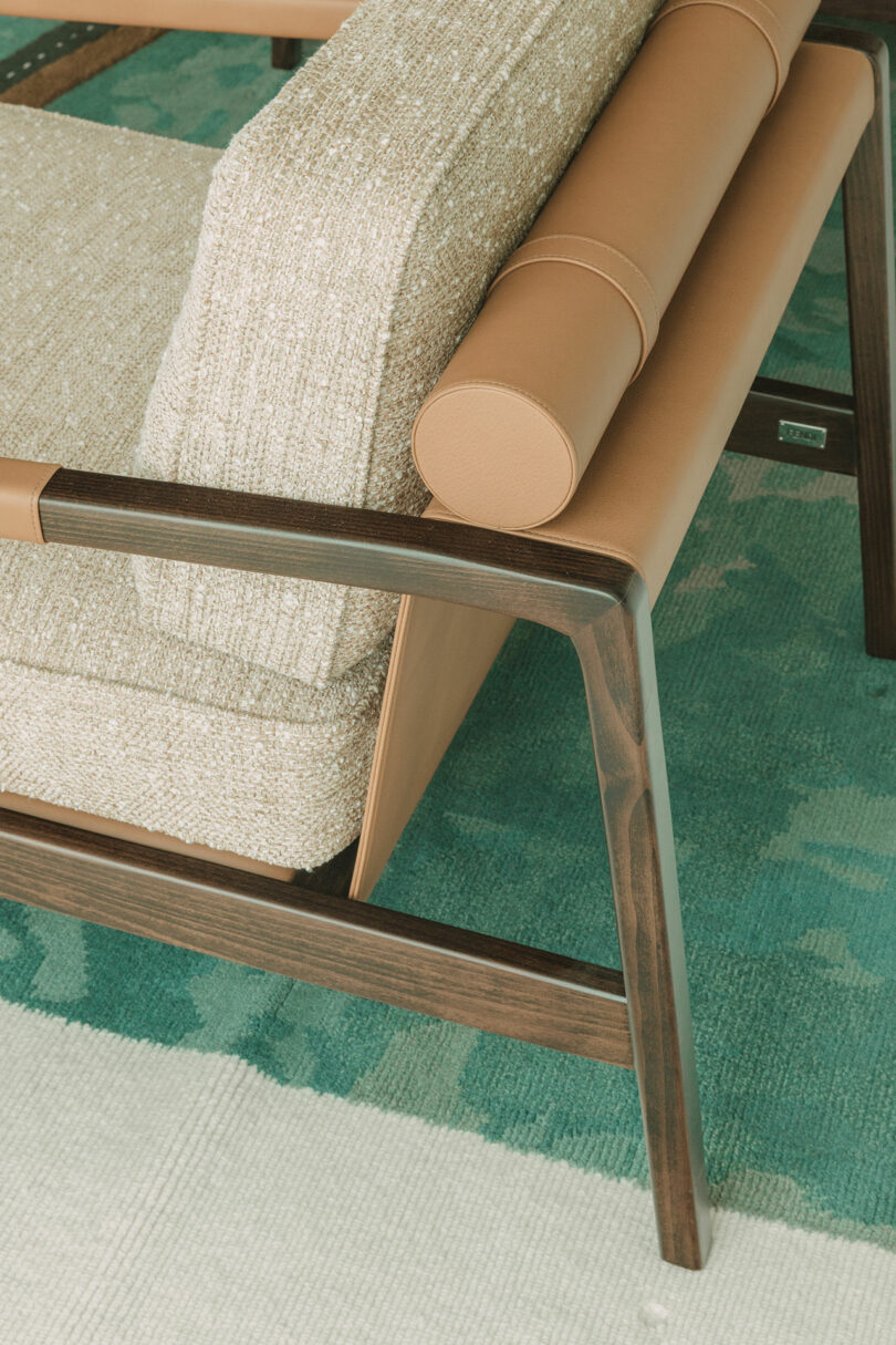 A wood-framed armchair with tan leather and textured cushions on a patterned rug.