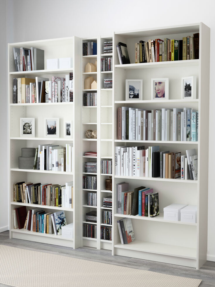 A tall, narrow white shelving unit filled with CDs standing between wider bookshelves.