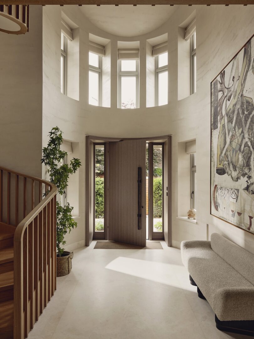 A modern three-story entryway with a wooden staircase, tall windows, and a large abstract painting.