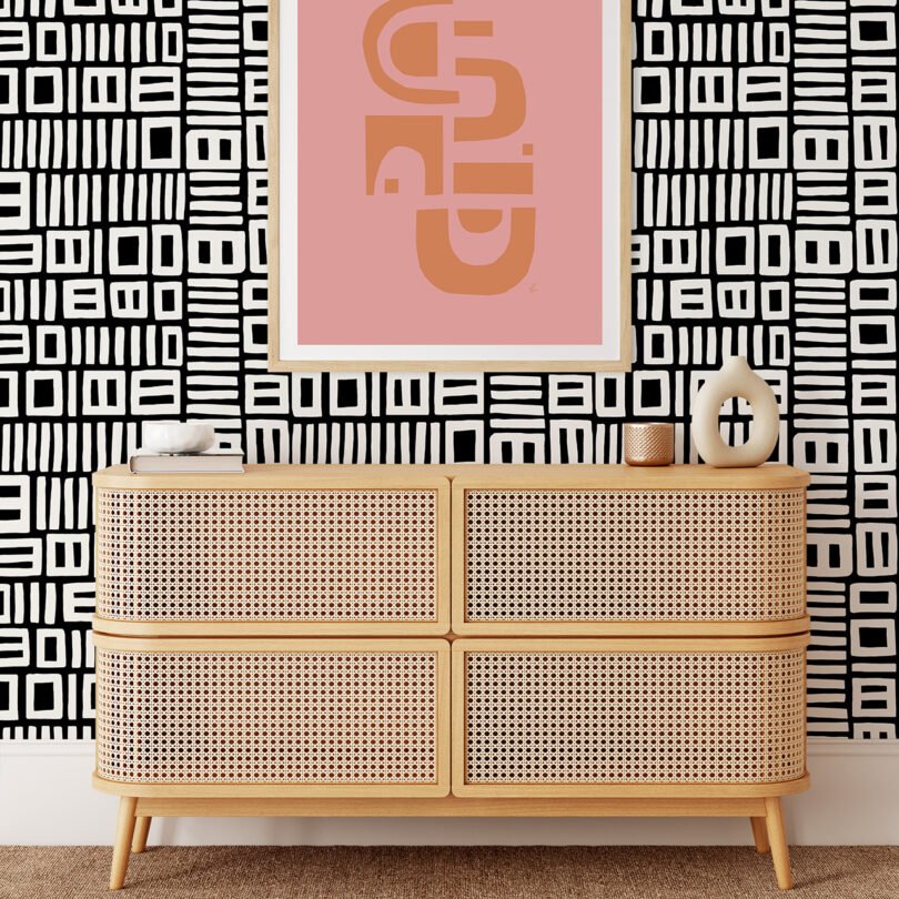 A light wood credenza against a wall with black and white patterned wallpaper.