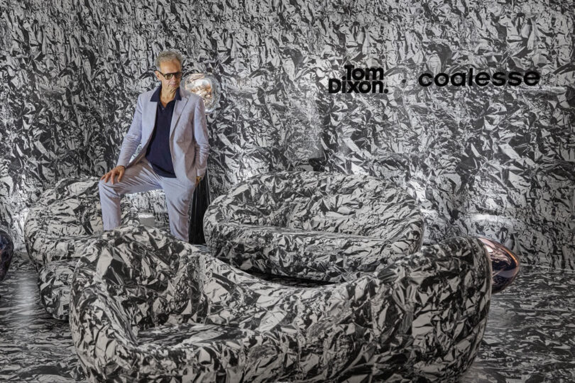 A man in a light suit standing in a room featuring the Tom Dixon and Coalesse branding and patterned wall coverings.