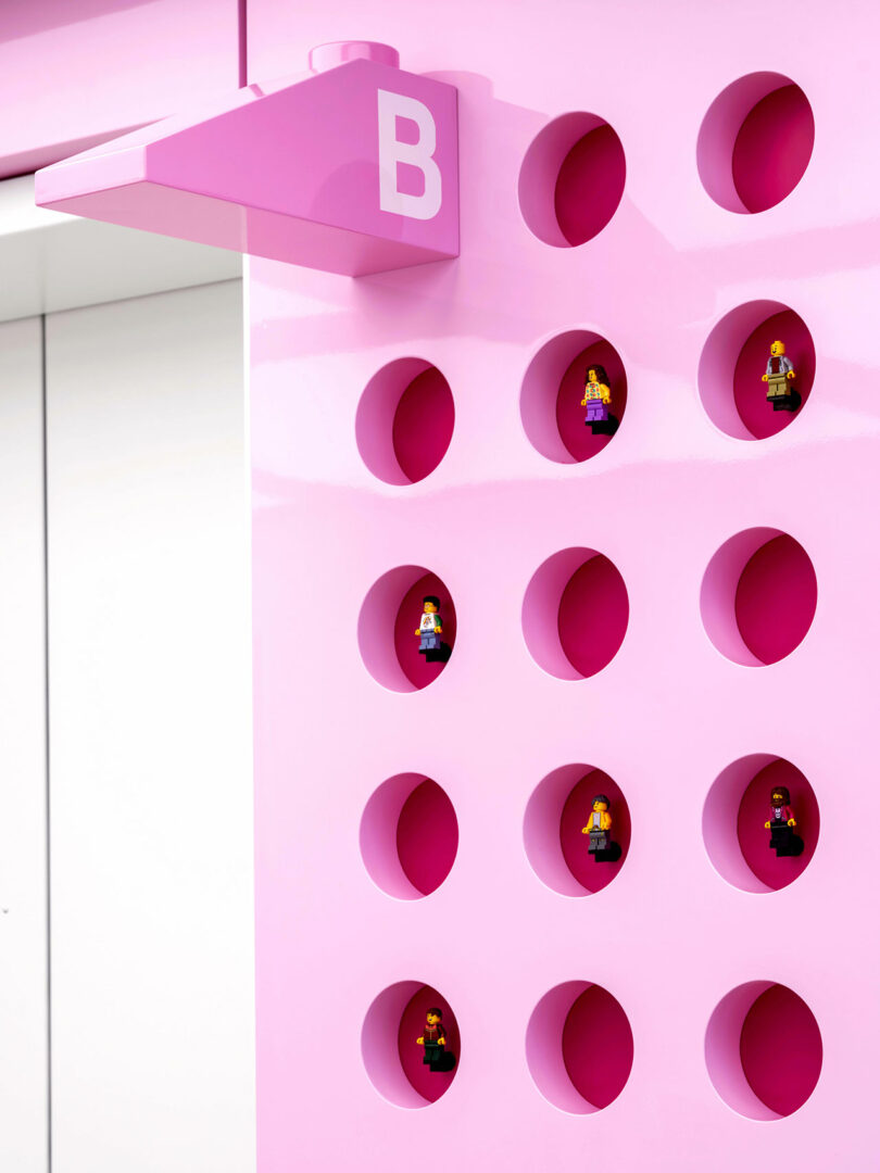 Close-up of a pink wall with circular cutouts displaying individual LEGO minifigures.