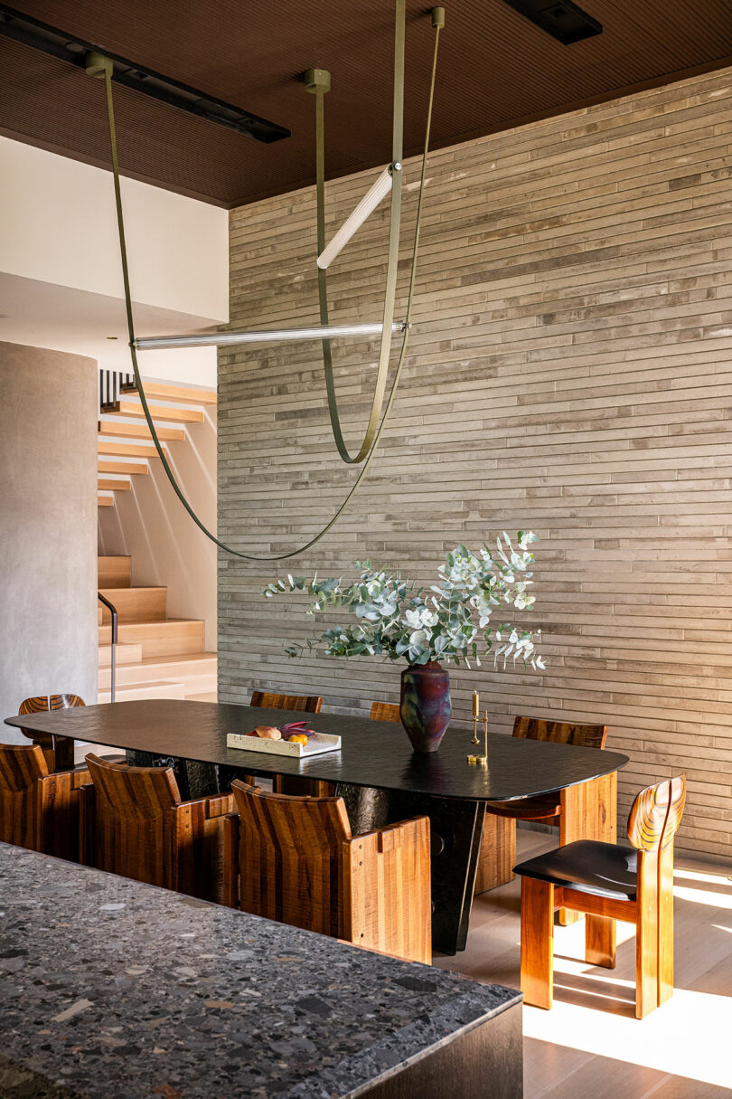 A dining room with a dark wooden table and a textured stone wall backdrop.