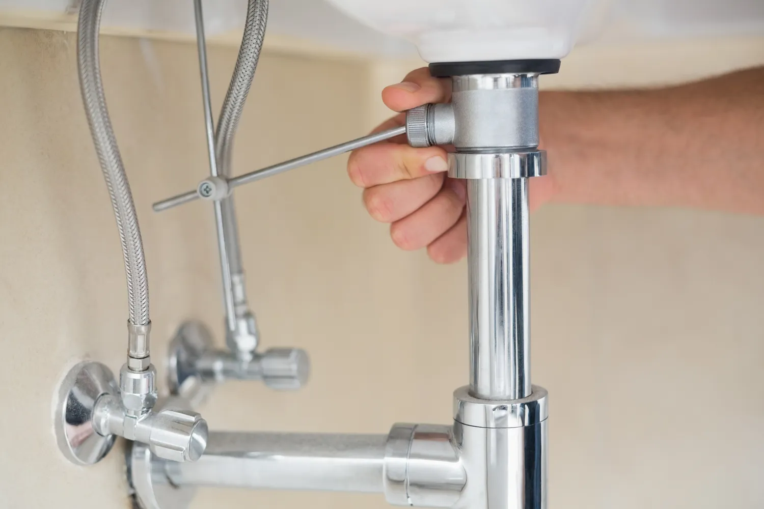 Internal view of a bathroom vanity cabinet showing the chrome P-trap, drain tailpiece, and water supply lines.