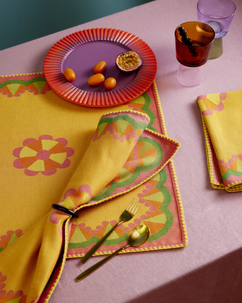 A purple Epin Rere plate with kumquats and gold cutlery on a pink tablecloth.