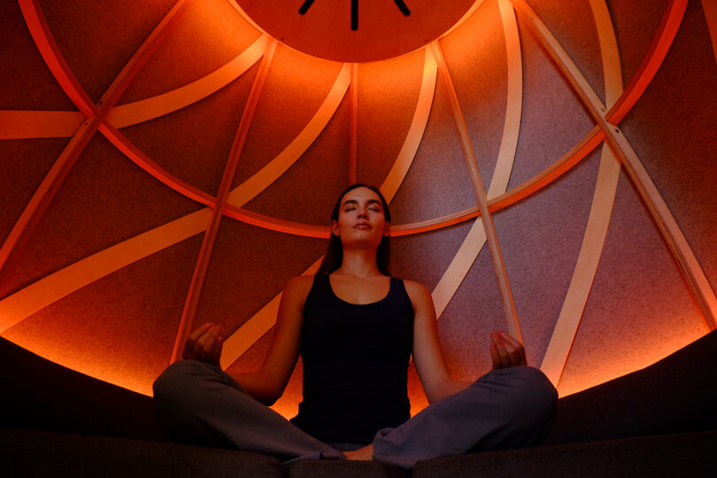 Interior view of an orange-lit dome ceiling with curved wooden beams during a meditation session.