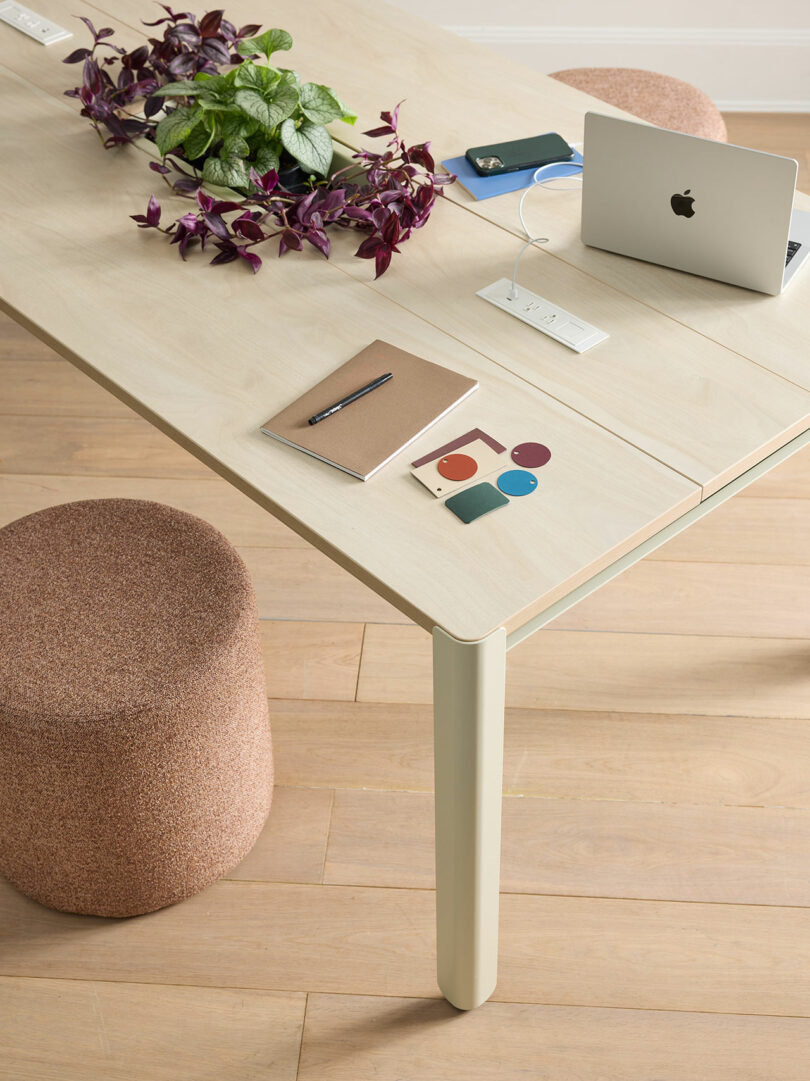 Close-up of a light wood table surface with a laptop, notebook, plant, and an integrated power charging hub.