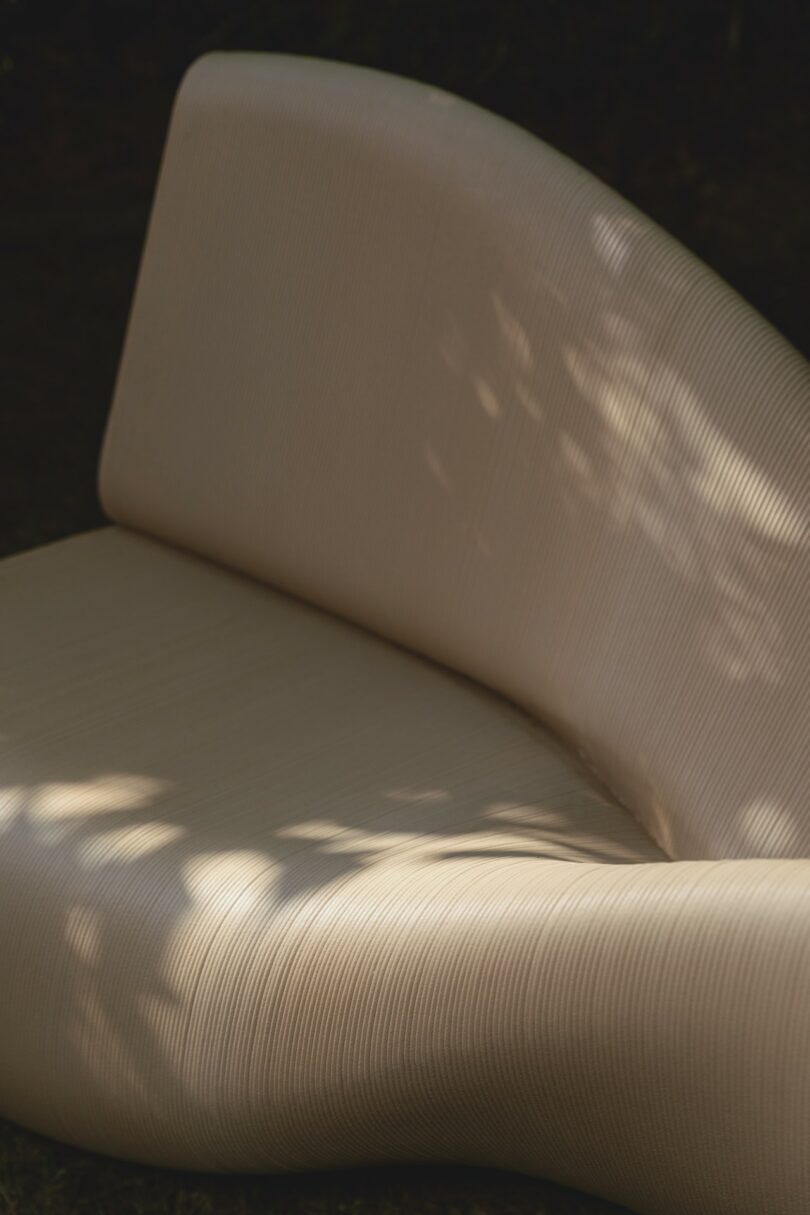 Close-up of a cream-colored curved bench showing the detailed 3D-printed ribbed texture in dappled sunlight.