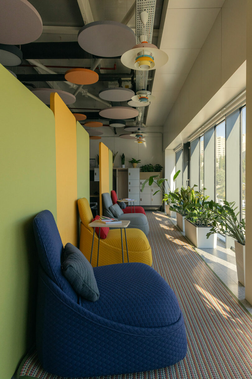 A seating area in an office with large windows, colorful dividers, and various potted plants on the windowsill.