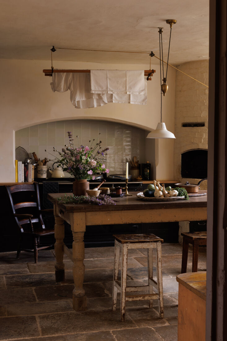 A long antique scullery table with oak post sections added to the legs for height, set against a Delft tile backsplash.