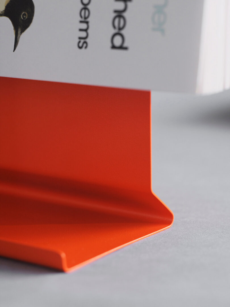 Close-up of a book resting on a bright orange metal bookend with a matte finish.