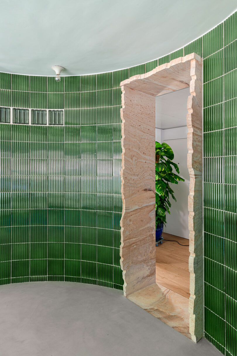 A contrast of glossy green tiles and a rough-textured natural stone portal leading to another room.