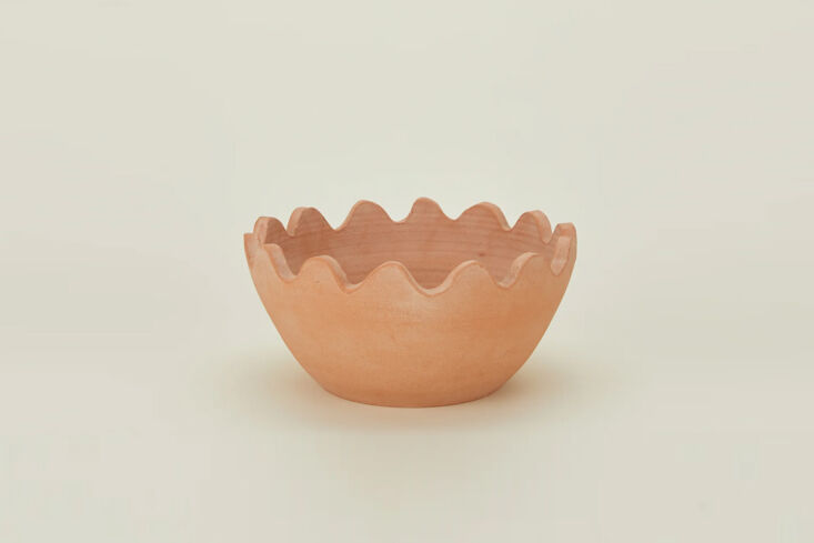 A terracotta serving bowl with a distinct scalloped rim, styled with fresh greens.