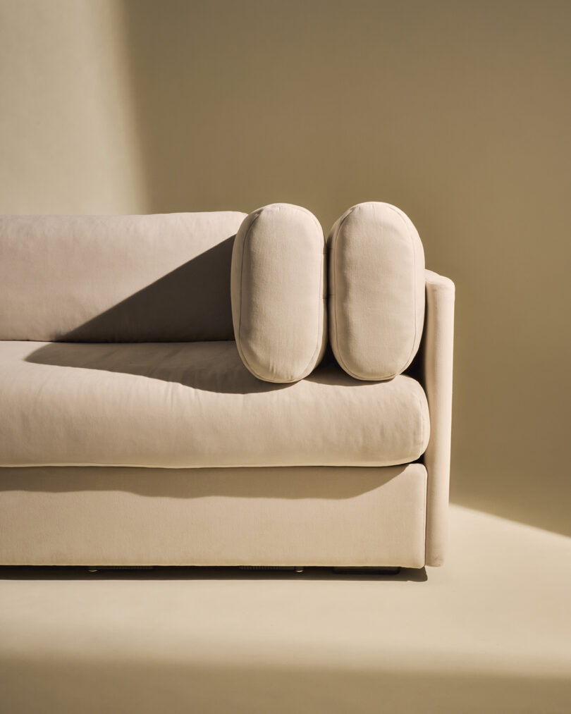 Detail of cylindrical cushions placed vertically on the armrest of a beige Elogio sofa.
