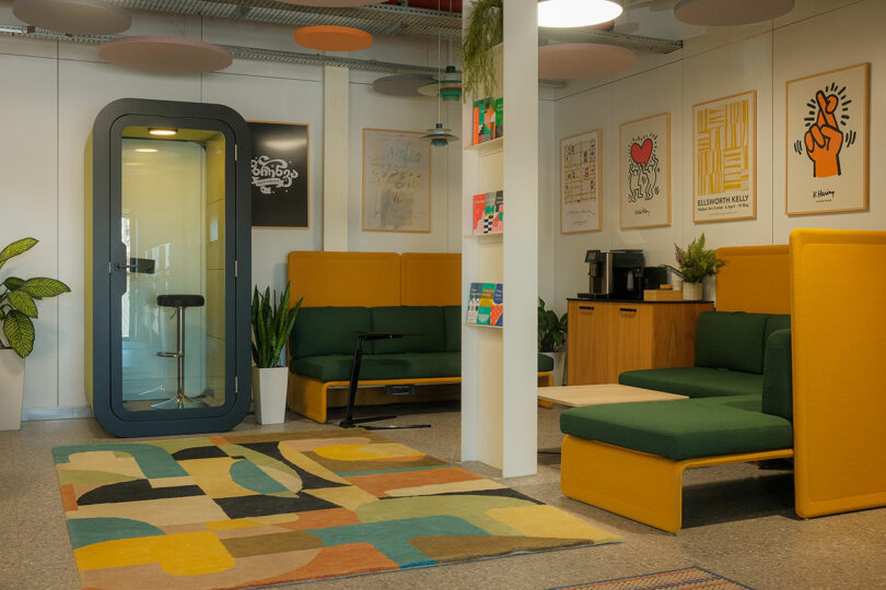 Office lounge area with green and mustard yellow seating, a colorful rug, and a private phone booth.