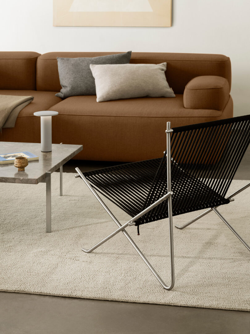 A modern living room featuring a brown sofa, marble table, and minimalist accent chairs.