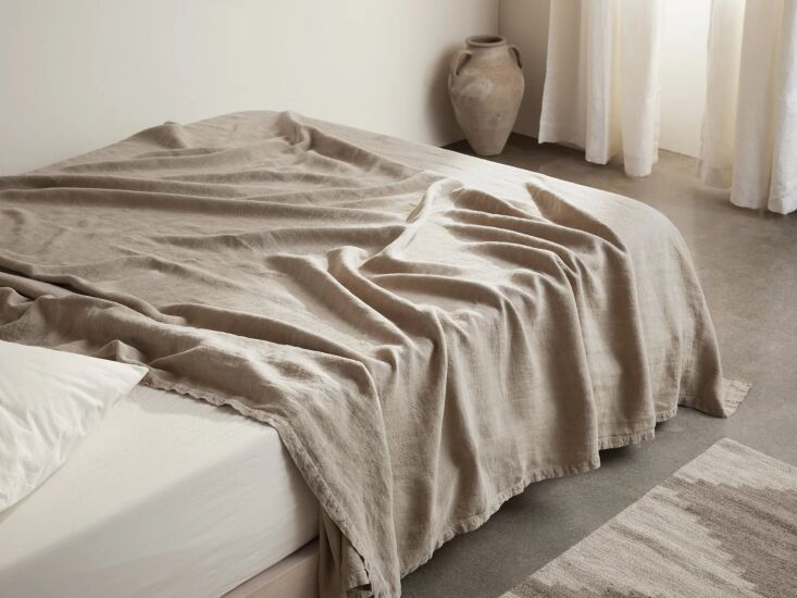 A vintage linen bed blanket in a natural flax color spread across a bed.