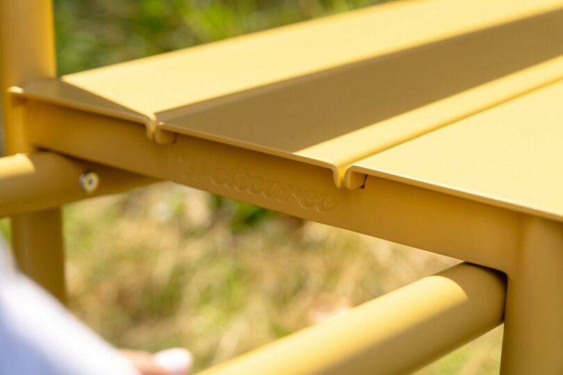 Close-up of the yellow metal frame of the bench with sunlight reflecting off the powder coating.