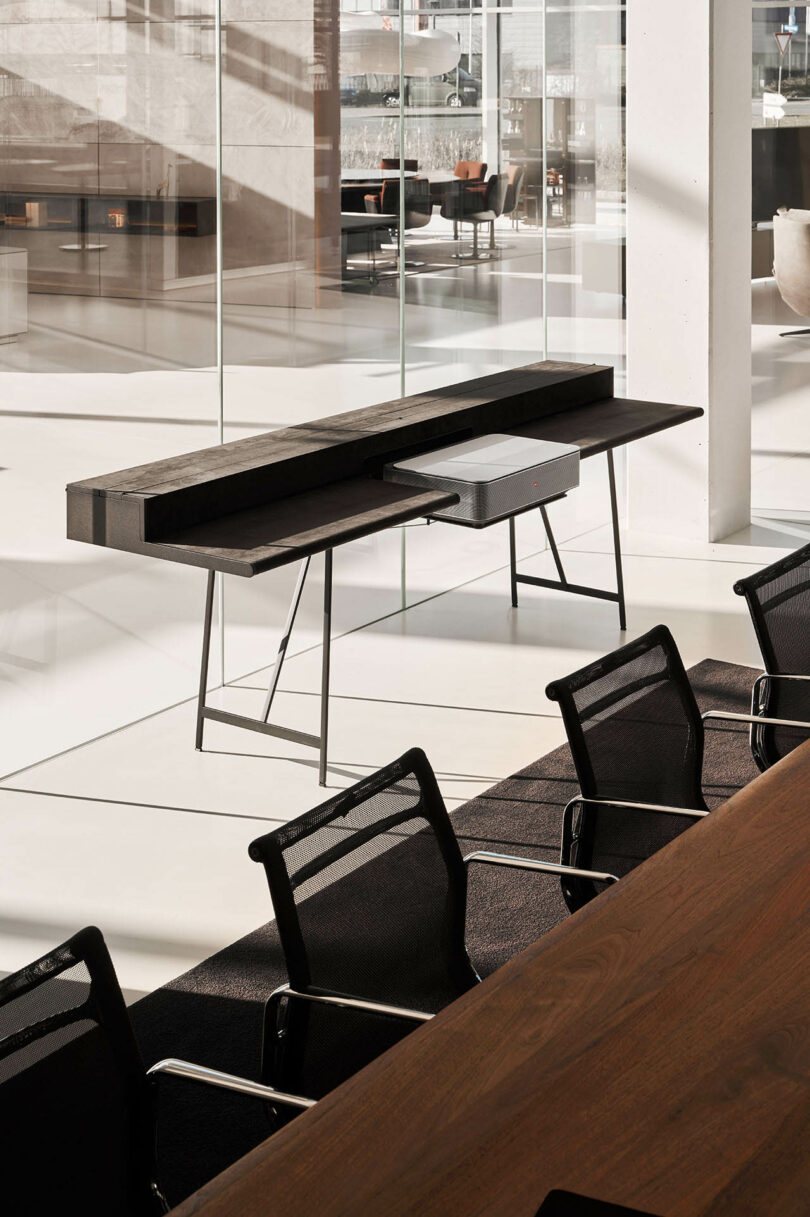 A minimalist console table positioned against a glass wall in a modern conference room with a wooden table.