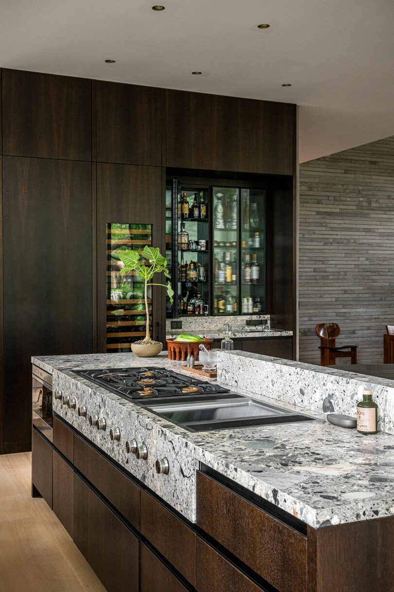 A modern kitchen featuring dark wood cabinetry and a large speckled granite island.