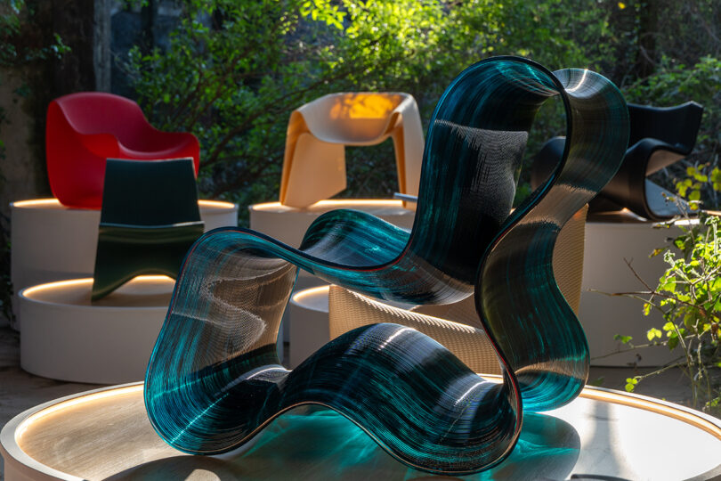 A wavy, translucent blue 3D-printed chair in the foreground of an exhibition space.