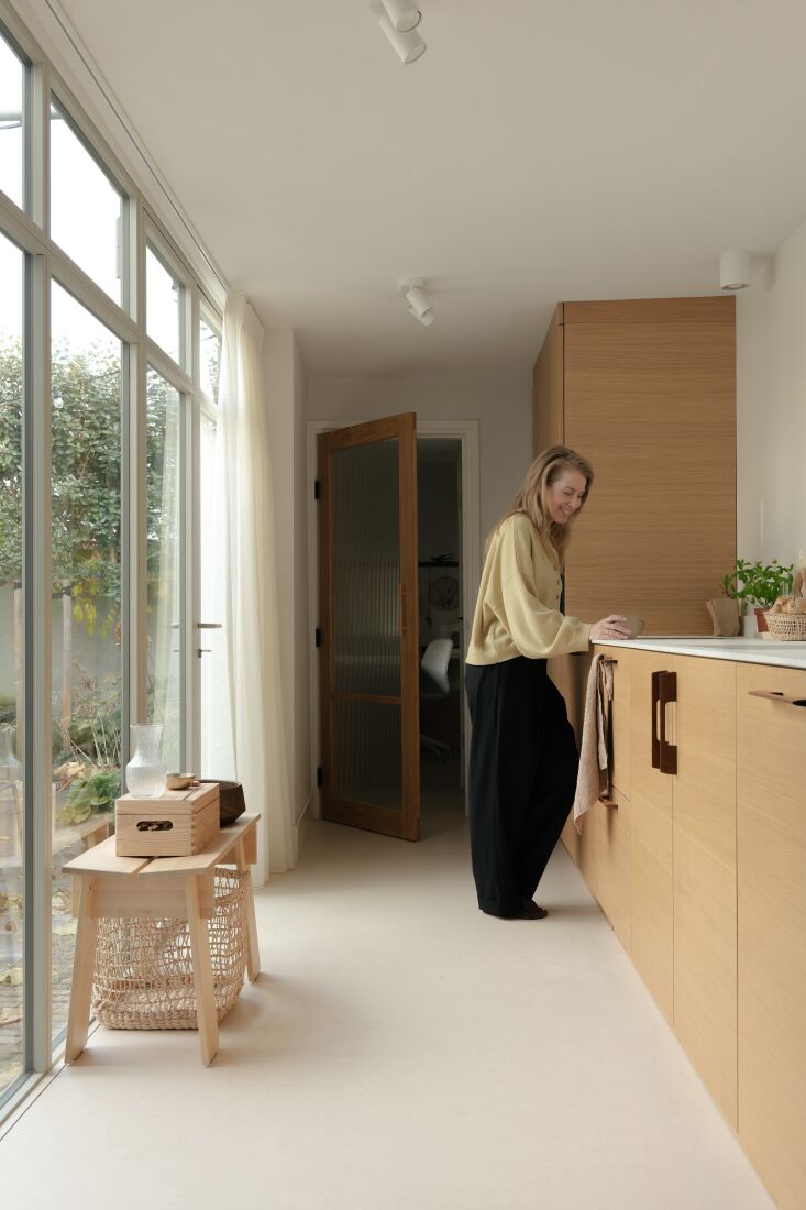 Designer Suzanne Pardijs standing in her kitchen next to a floor-to-ceiling black steel-framed window wall.