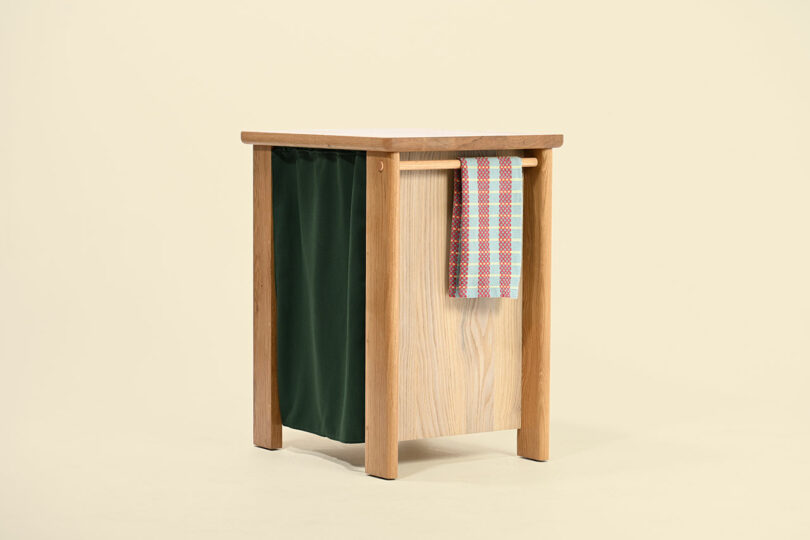 A wooden side table featuring a built-in green fabric storage pocket and draped colorful cloth.