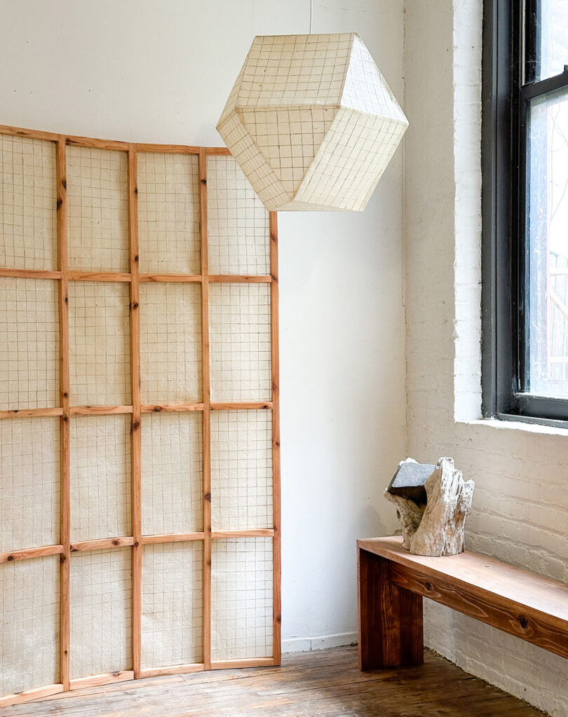A minimalist living space featuring geometric paper lighting, a folding screen, and natural wood furniture.