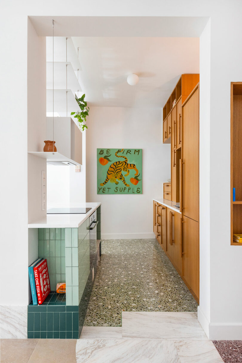A modern kitchen with green tiles, wooden cabinets, and a colorful artwork of a tiger with the text 'Be firm yet supple'.