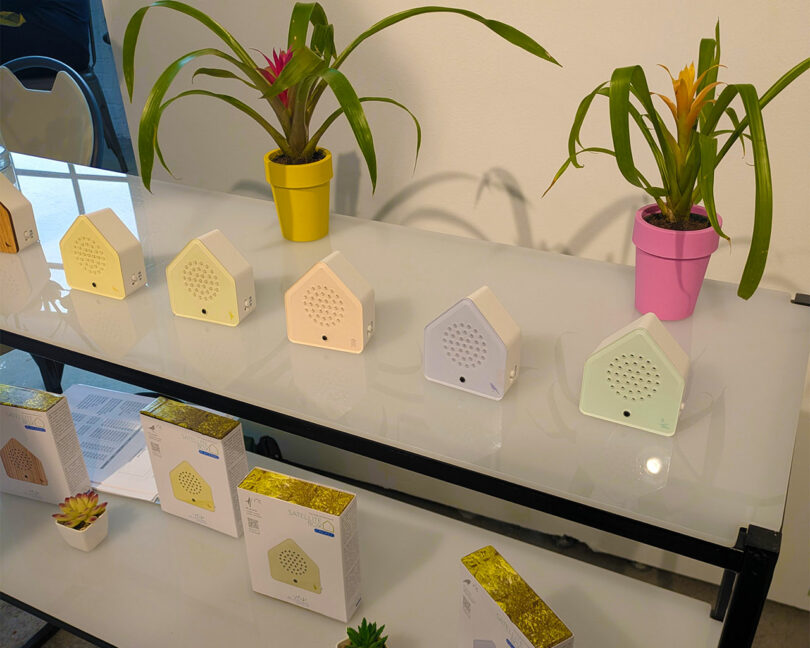 A row of small house-shaped electronic devices on a display table with plants.