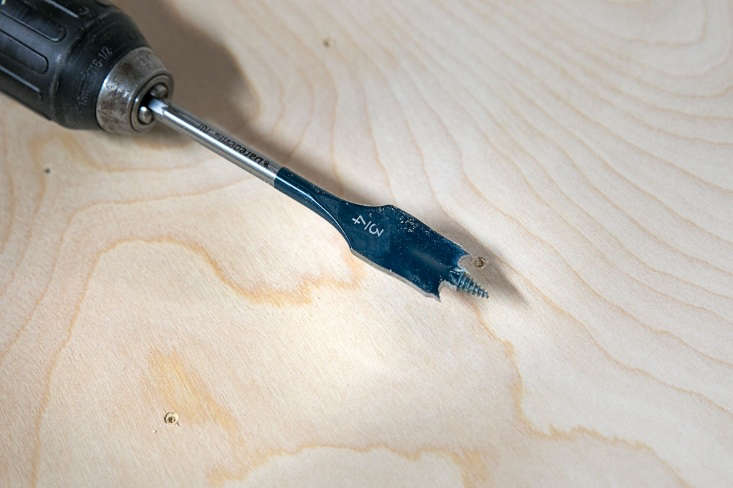 Macro view of small pilot holes marked on a wood board for a pegboard grid.