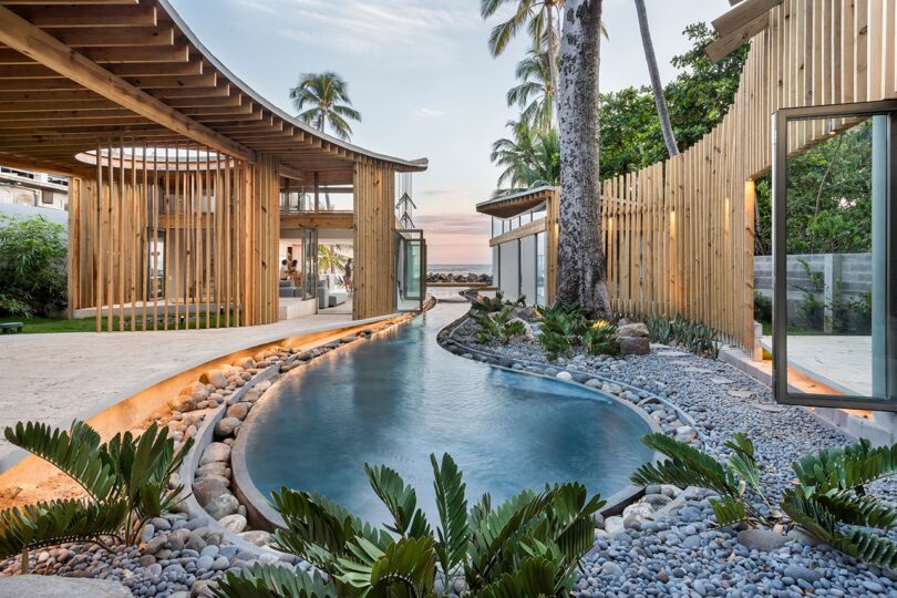 A luxury beachfront villa with wooden architecture and a long pool at sunset.