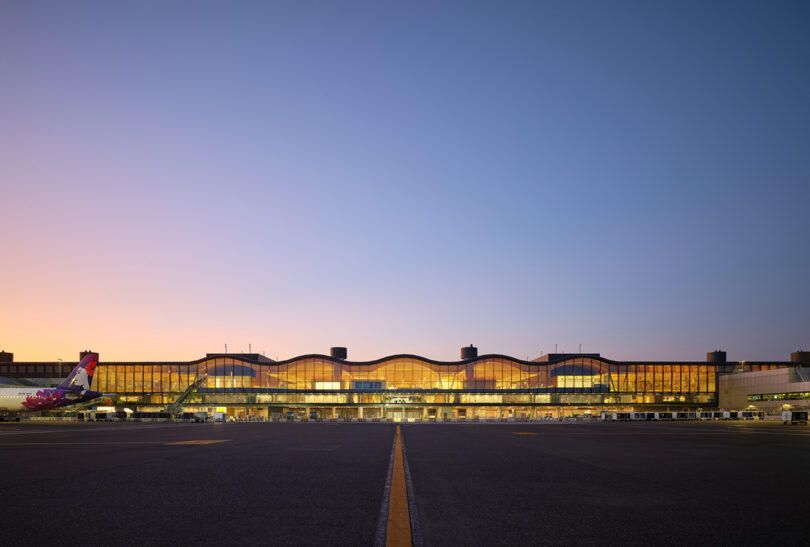 The illuminated exterior of the PDX terminal at dusk with an airplane parked at the gate.