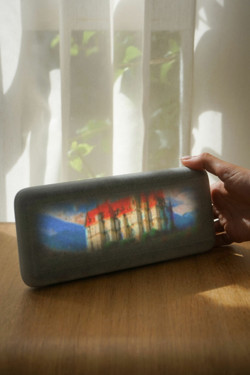 A hand holds the Dream Recorder device showing a blurred, dreamy image of a red-roofed building.