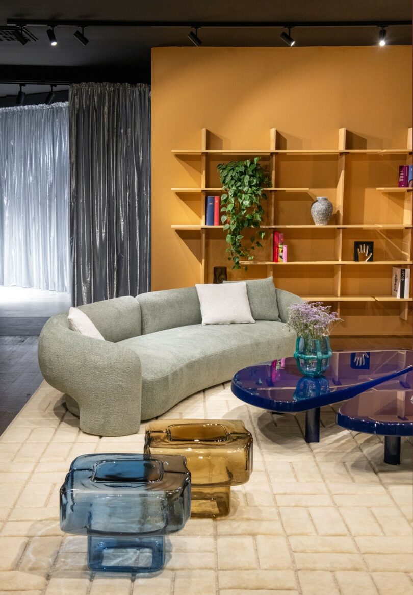 A modern living room with a green curved sofa and blue glass stools used as sculptural furniture.