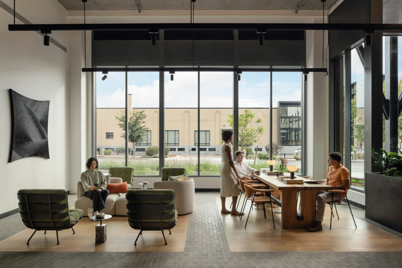A modern office lounge with high ceilings, large windows, and large indoor plants where people are collaborating.
