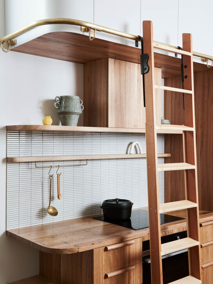Close-up of a wooden rolling library ladder attached to high kitchen cabinetry.