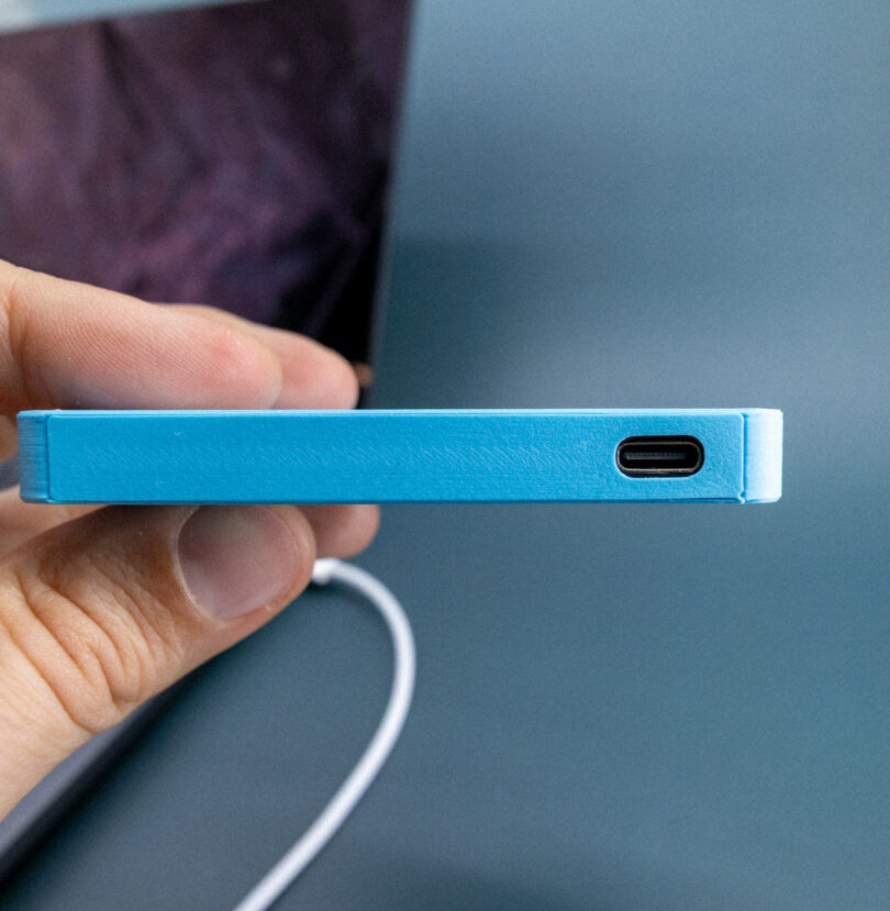 A person's hand holding the FolderDrive to show the USB-C port located on the bottom edge.