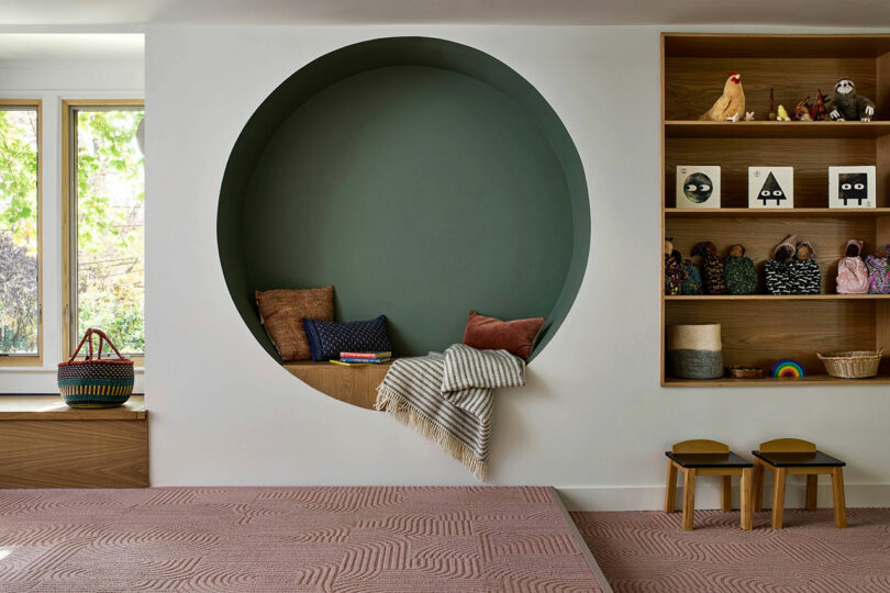 A cozy circular wall nook with cushions and blankets integrated into a room with minimalist wooden furniture.