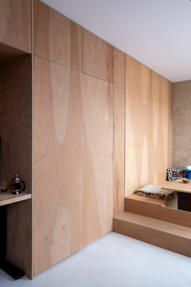 Close-up of light wood wall panels and a built-in bench with a French press on a shelf.