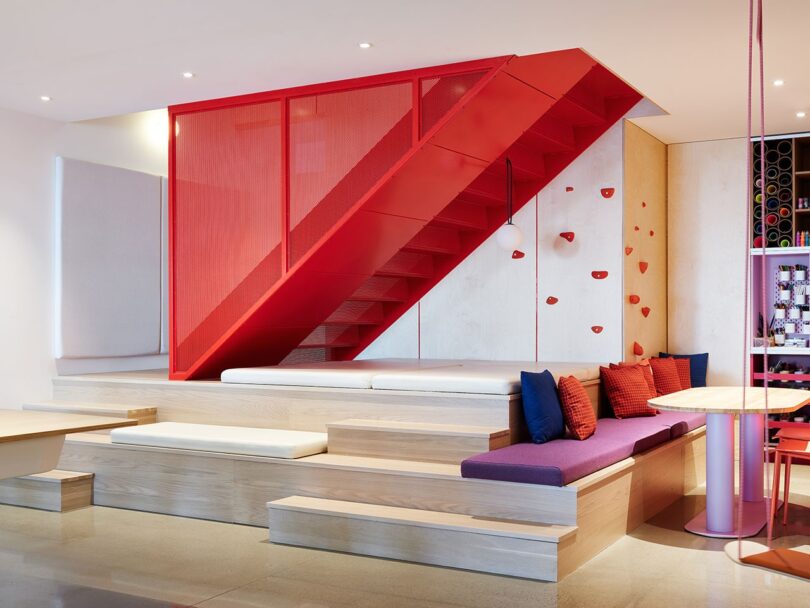 A vibrant indoor space featuring a bold red staircase and a rock climbing wall.