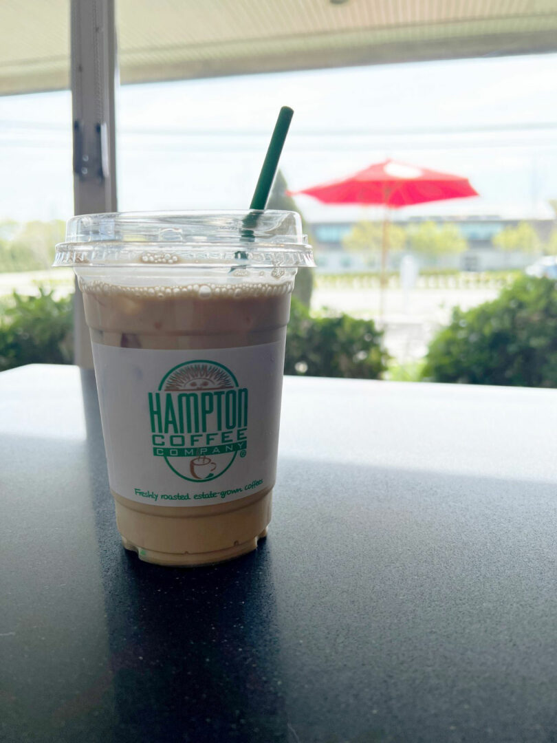 An iced coffee with a green straw from Hampton Coffee Company on a table.