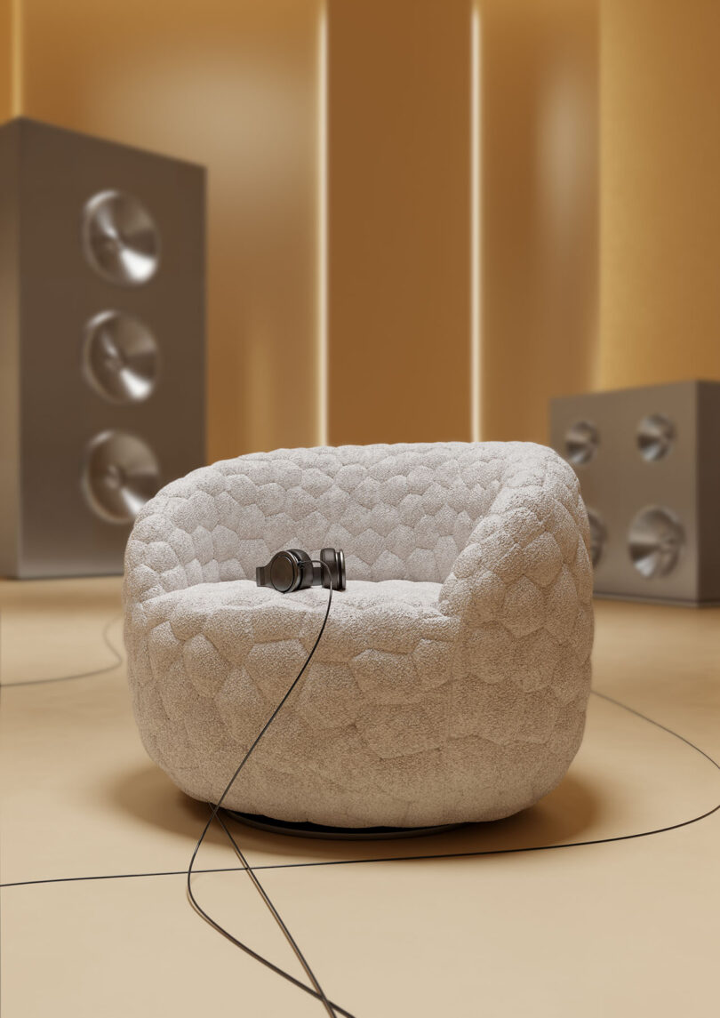 A white Introvert Chair in a room with large speakers and headphones resting on the seat.