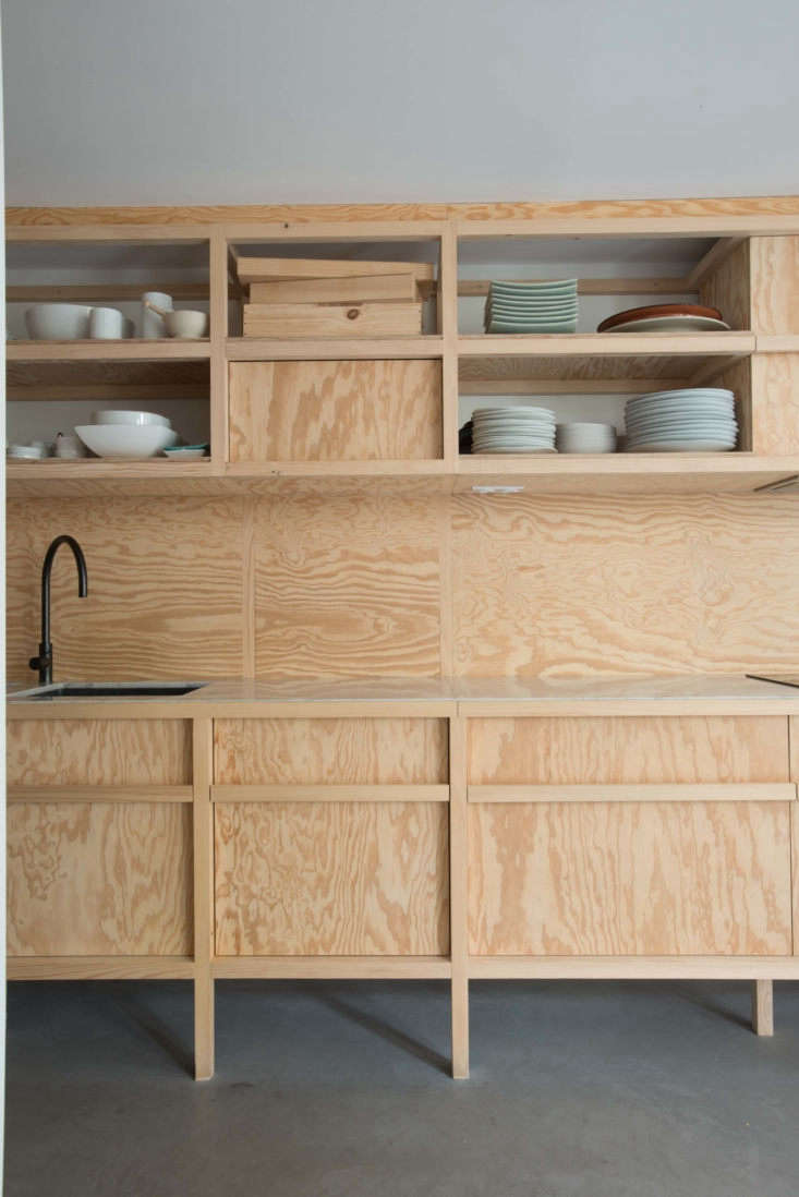 A minimalist kitchen featuring pine plywood cabinets, a marble countertop, and a matte black faucet.