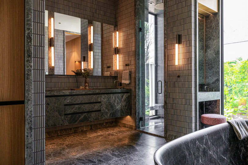 Luxury bathroom with dark marble flooring, a freestanding tub, and views of outdoor greenery.